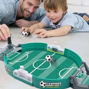 Man and child playing with a miniature football table game on a light-colored surface.